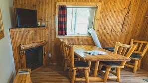 A wooden cabin interior with a fireplace, a dining table with chairs, a television, and a window with curtains. - 3BR Lakefront Cabin w/ Private Launch & Dock (Backus)
