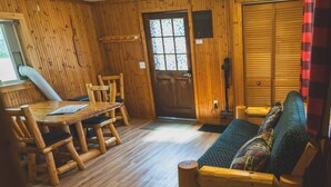 A wooden cabin interior with a dining table, chairs, a sofa, and a door. - 3BR Lakefront Cabin w/ Private Launch & Dock (Backus)