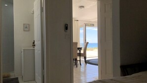 Une chambre avec un lit, un petit coin cuisine et une vue sur la plage par une porte ouverte.