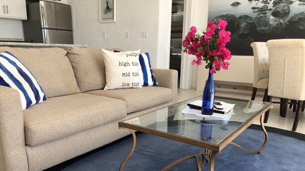 Un soggiorno con un divano color beige, un tavolino in vetro e un vaso blu con fiori rosa.