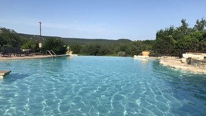 Ein klares Schwimmbecken mit Stufen, umgeben von Liegestühlen und Blick auf Hügel im Hintergrund.