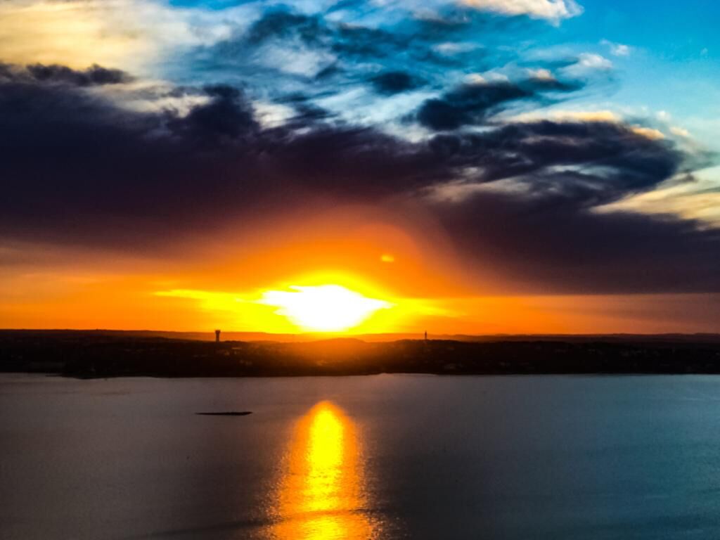Een zonsondergang boven een rustig wateroppervlak met het silhouet van een gebouw in de verte.