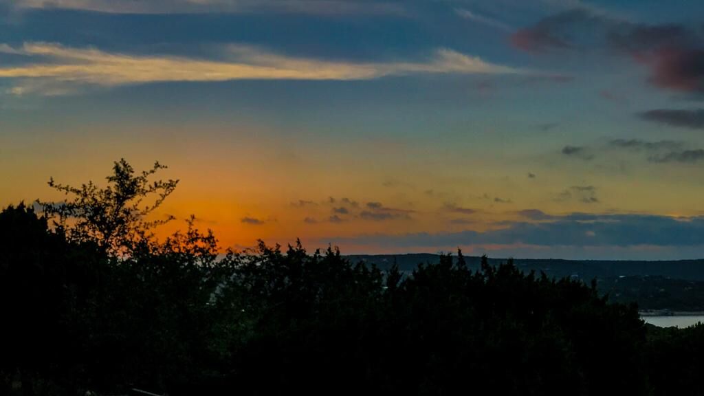 Un coucher de soleil sur un paysage boisé, avec une étendue d’eau visible au loin.