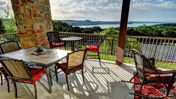 Ein Balkon mit einer Steinsäule, einem Tisch mit Stühlen und Blick auf einen See und Berge.