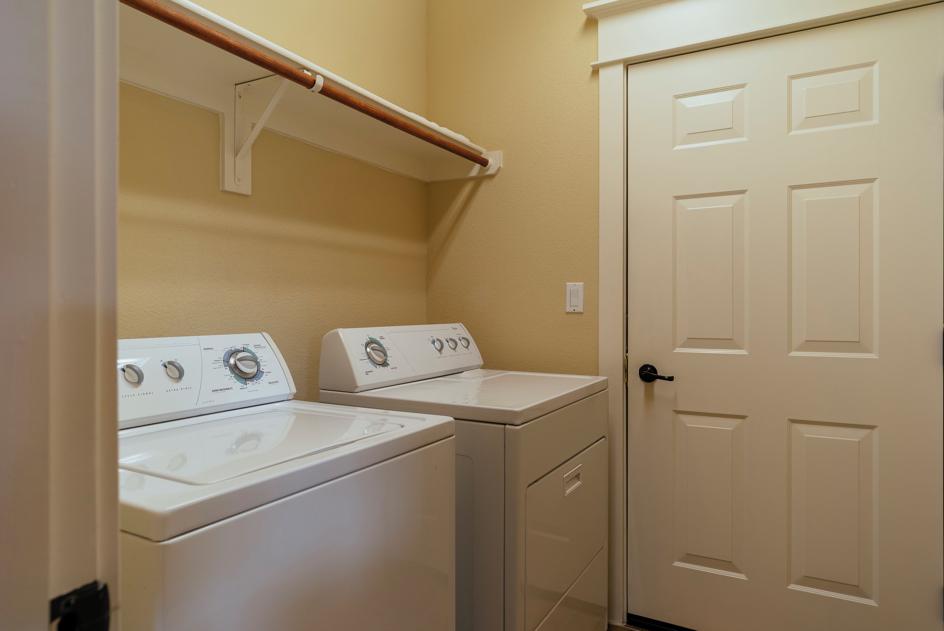 A laundry room with two white washers and dryers, a wooden towel rack, and a white door.
