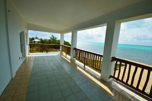A covered balcony with a view of the ocean, white pillars, and a tiled floor. - Sea The View, Ocean Front (San Pedro)