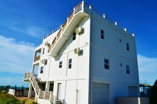 A multi-story building with a staircase leading to a balcony, a garage, and a clear view of the sky.