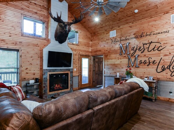 A cozy log cabin interior with a fireplace, leather sofa, and a mounted moose head.