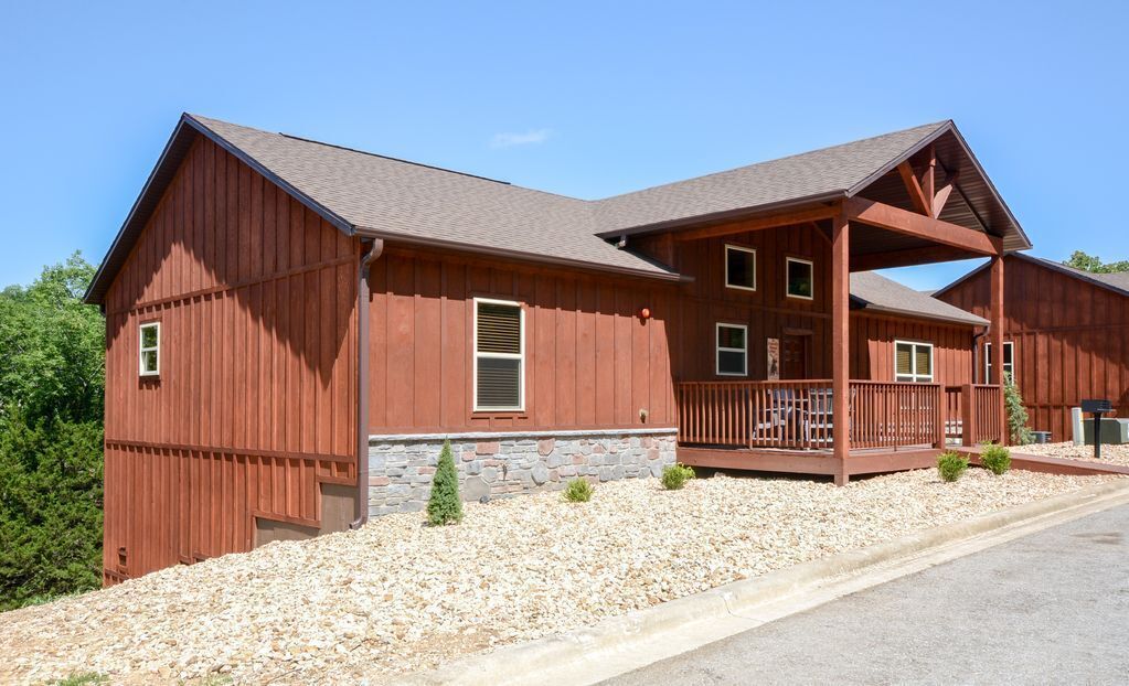 A red wooden house with a stone foundation, a porch, and a small garden area.