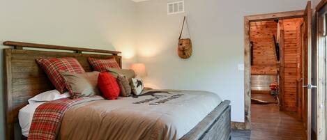 A bedroom with a wooden bed, a ceiling fan, a wall-mounted lamp, and a door leading to a wooden room.