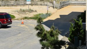 Un área de estacionamiento con una camioneta SUV roja, una cerca de madera y una playa al fondo.