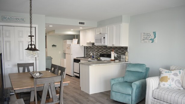 Una cocina moderna con armarios blancos, una isla central y un comedor con mesa y sillas de madera.