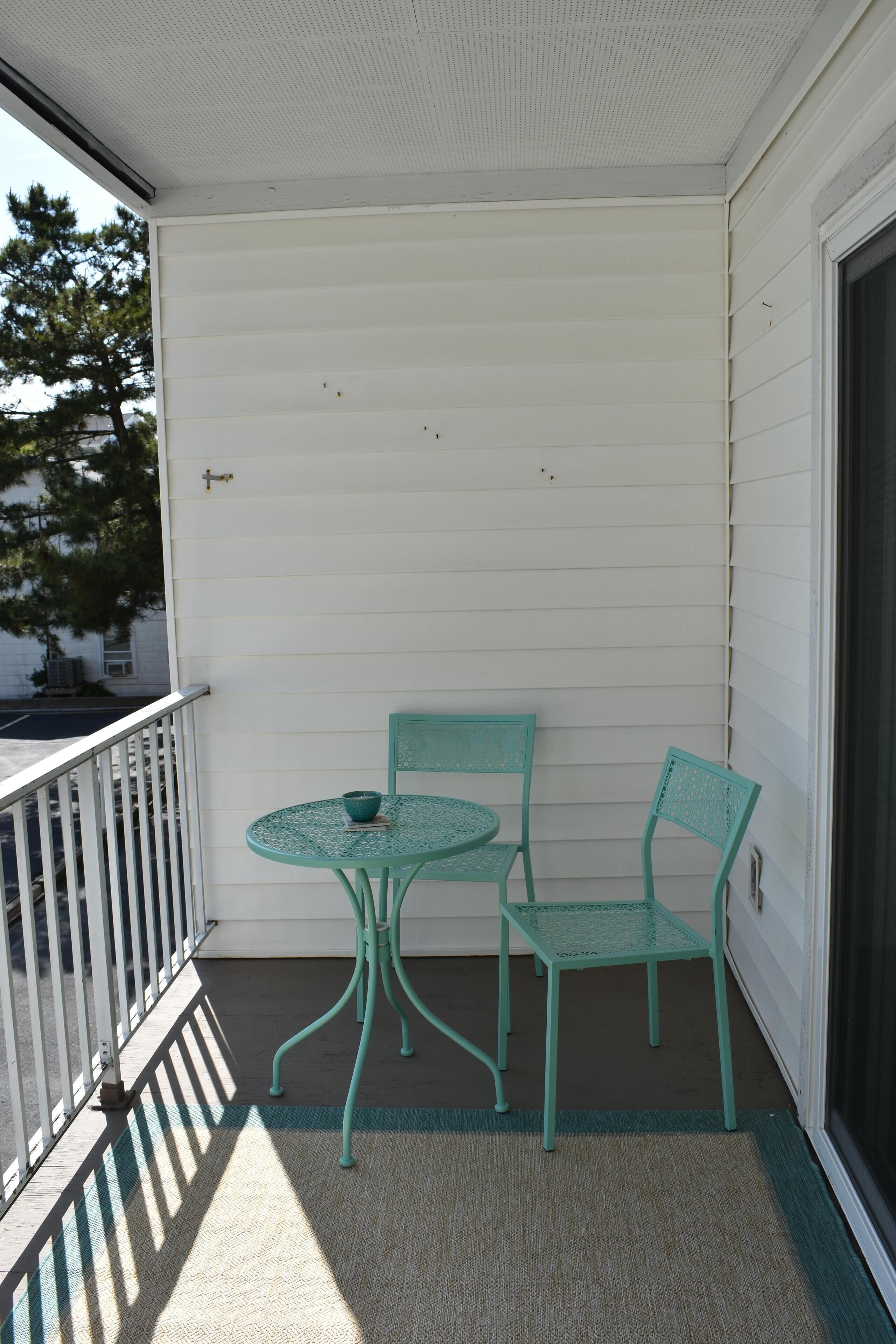 A balcony with a small table and two chairs, a white exterior wall, and a door.