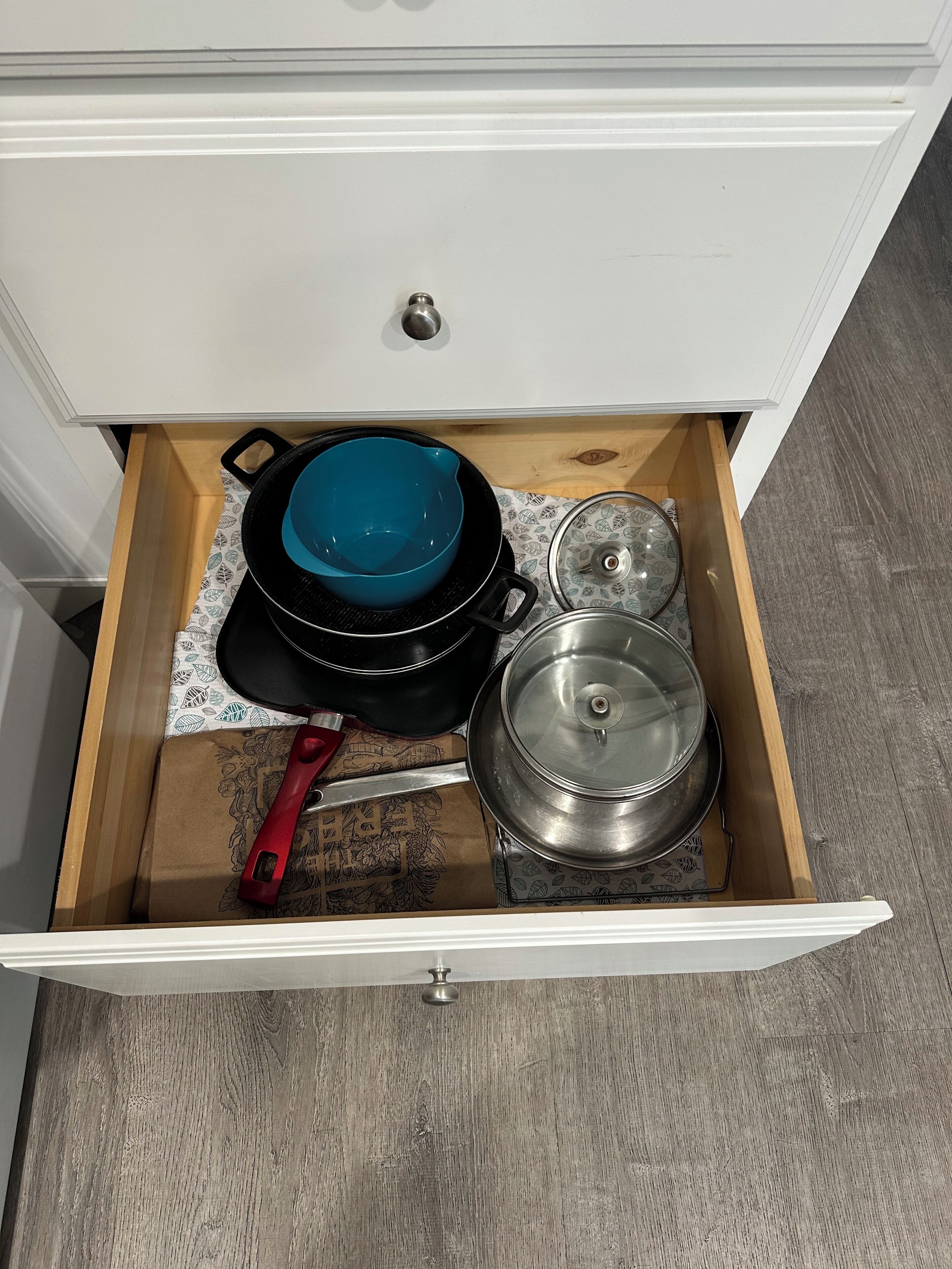 A kitchen drawer with a blue pot, a red-handled pan, and a covered pot.