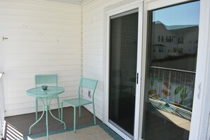 Un petit balcon avec deux chaises en métal turquoise et une petite table, une porte-fenêtre coulissante et une vue sur un quartier résidentiel.