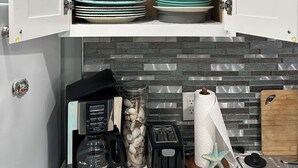Una cocina con cafetera, tostadora y un tarro de conchas marinas sobre la encimera.
