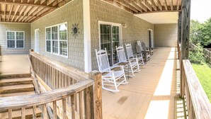 A covered porch with wooden railings, white rocking chairs, and a brick exterior. - Sand Castle, 9 bedroom,6 1/2 bath,sleep 26,  pool, hottub, elevator, beach close (Oak Island)