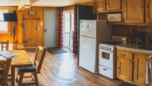 Un interior de madera con una mesa de comedor, sillas, una cocina que incluye estufa, refrigerador y armarios de madera.