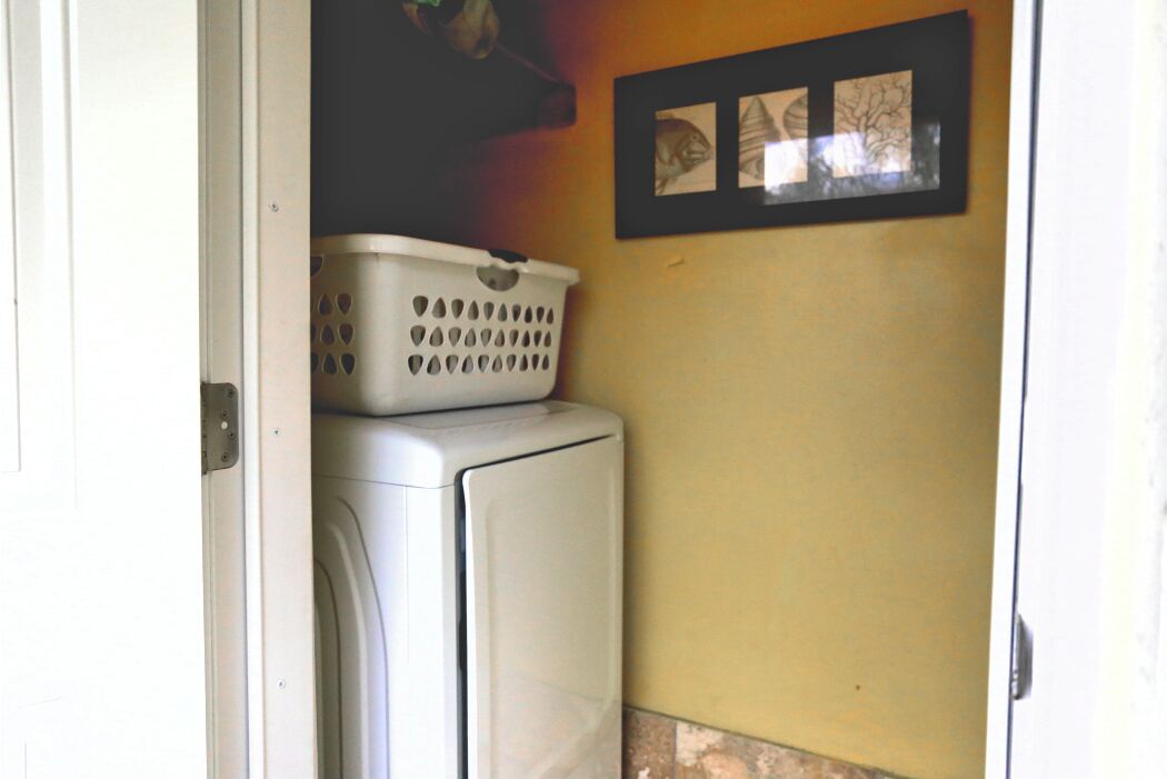 Una sala de lavandería con una lavadora y una cesta blanca de ropa encima.