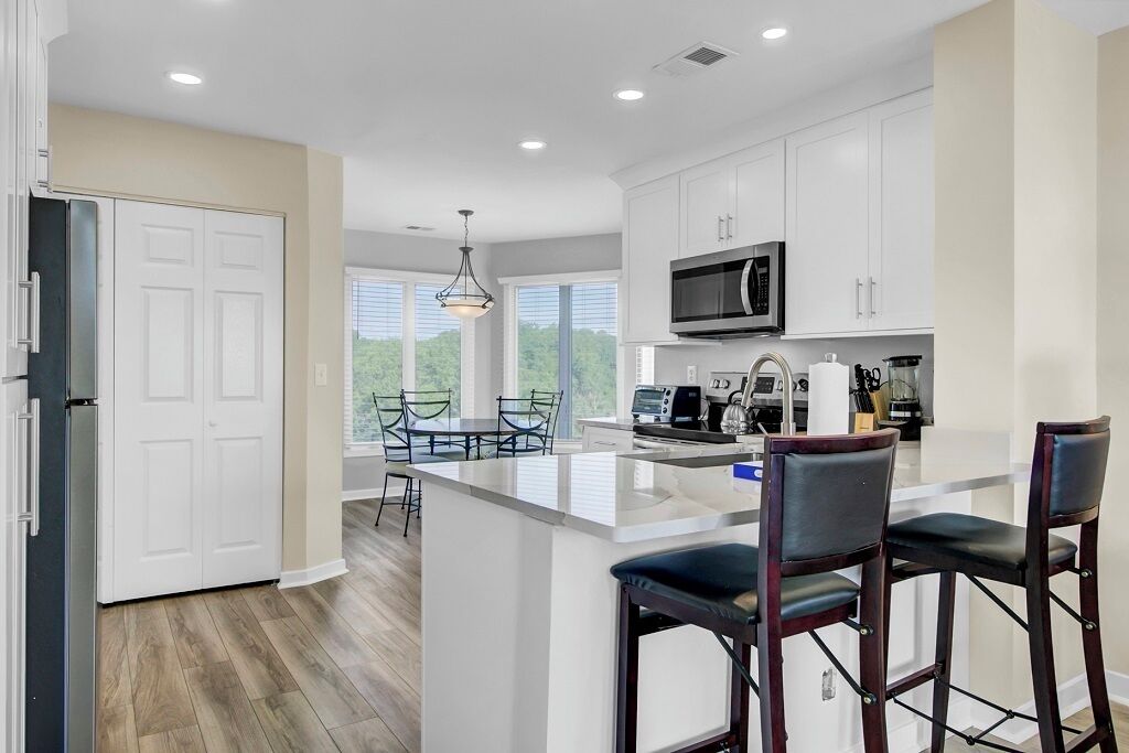 A modern kitchen with white cabinets, a large island with bar stools, a microwave, and a coffee maker.