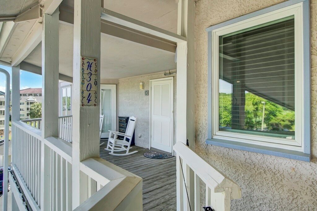 A covered porch with a wooden floor, a rocking chair, and a sign with numbers.