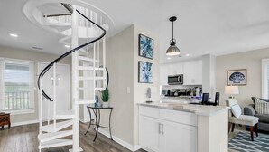 A modern kitchen with white cabinetry, a central island, and a spiral staircase. - Award-Winning Resort Amenities | Tidewater H304 (Isle of Palms)
