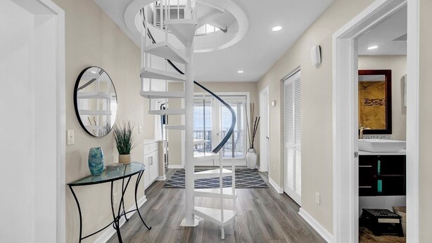A modern interior with a spiral staircase, a round mirror, and a glass table with a plant. - Award-Winning Resort Amenities | Tidewater H304 (Isle of Palms)