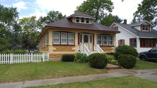 A two-story house with a front porch, a picket fence, and a well-maintained lawn.