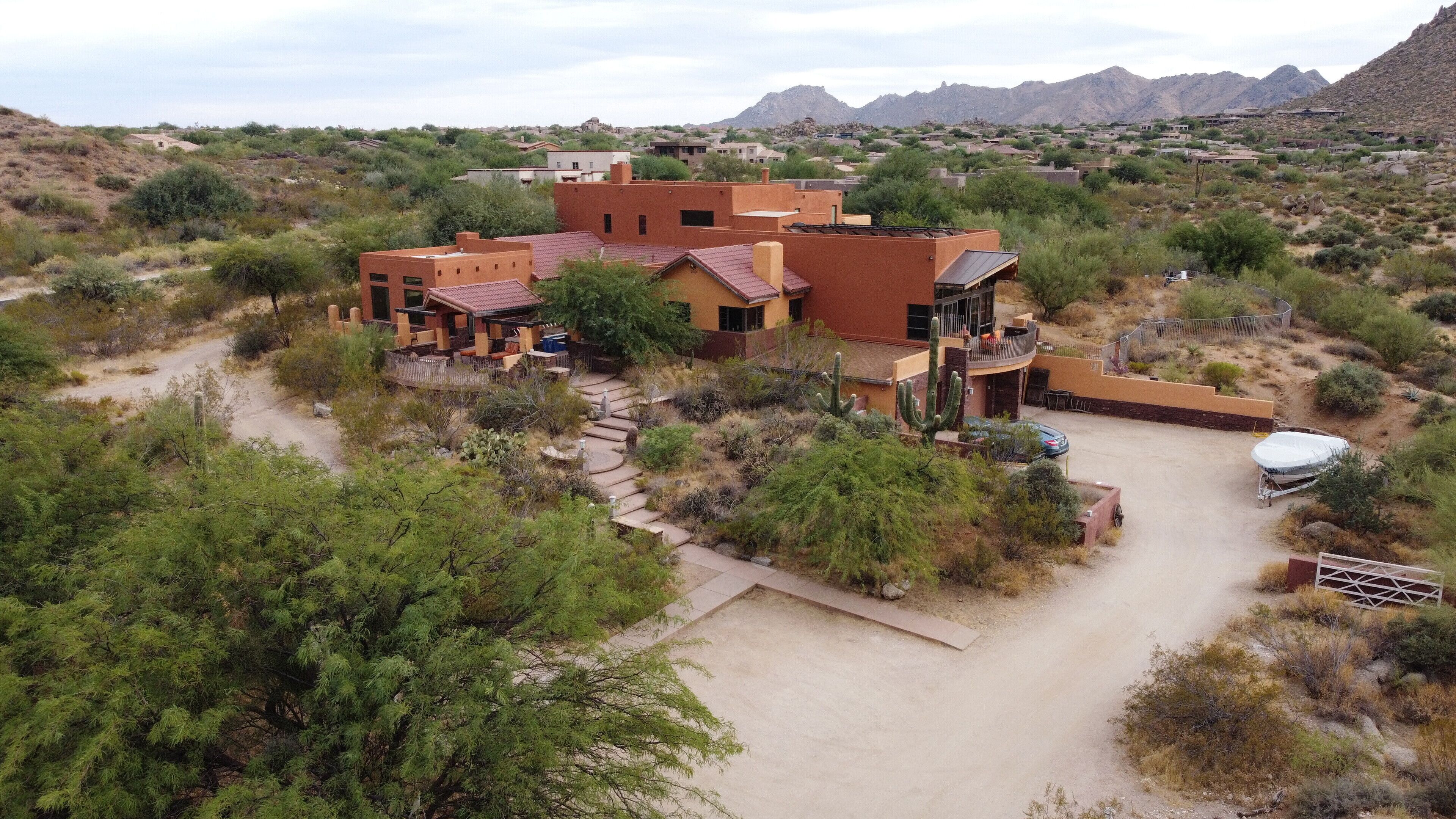 A large, multi-story building with a flat roof, surrounded by desert vegetation and mountains in the background.