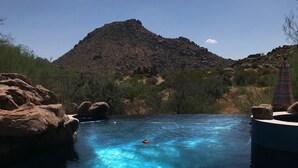 Ein klares, blaues Schwimmbecken mit Blick auf eine Bergkulisse, umgeben von felsigem Gelände und vereinzelter Vegetation.