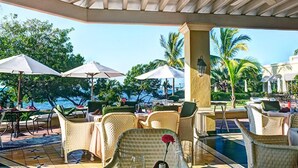 A covered outdoor seating area with wicker furniture, umbrellas, and a pool.