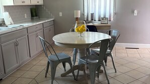 Une cuisine avec une table à manger, des chaises, un ventilateur de plafond et une fenêtre avec des rideaux.