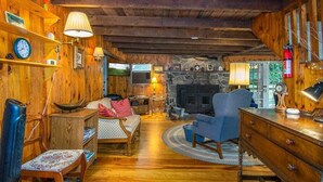 Ein gemütliches Blockhaus-Interieur mit Holzwänden, einem Kamin aus Stein, einem blauen Sessel und einem Holzesstisch.