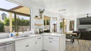 A modern kitchen with white cabinetry, a large window, and a dining area with a gray chair and a black and white rug. - SWSS 5BR Kierland-Area Luxury Home | Heated Pool, Putting Green & Outdoor Living (Scottsdale)