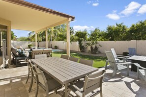 Um pátio externo com mesa e cadeiras de madeira, piscina e área de estar coberta.