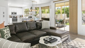 A modern living room with a dark leather sofa, a coffee table, and a kitchen in the background. - SWSS 5BR Kierland-Area Luxury Home | Heated Pool, Putting Green & Outdoor Living (Scottsdale)