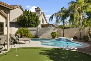 Um quintal com piscina, um alpendre com mobiliário para área externa e gramado bem cuidado.