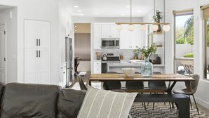 A modern kitchen with white cabinets, a wooden dining table, and a black sofa with a striped pillow. - SWSS 5BR Kierland-Area Luxury Home | Heated Pool, Putting Green & Outdoor Living (Scottsdale)
