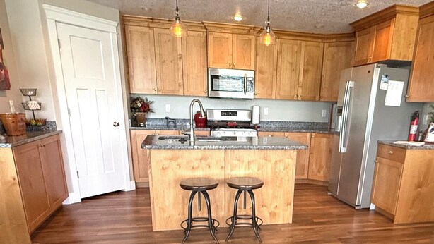 A kitchen with wooden cabinets, a stainless steel refrigerator, a microwave, and two stools. - All One Level Basement Unit Large Great Room Kitchen 3 bed 2 baths (Lava Hot Springs)