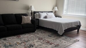 A bedroom with a bed, a dark-colored sofa, a patterned rug, and a ceiling fan. - All One Level Basement Unit Large Great Room Kitchen 3 bed 2 baths (Lava Hot Springs)