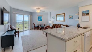 A spacious living area with a large island, a dining table, and a view of the outdoors.