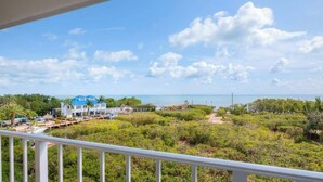 A view from a balcony overlooking a coastal area with a clear sky, a beach, and a resort with blue-roofed buildings.