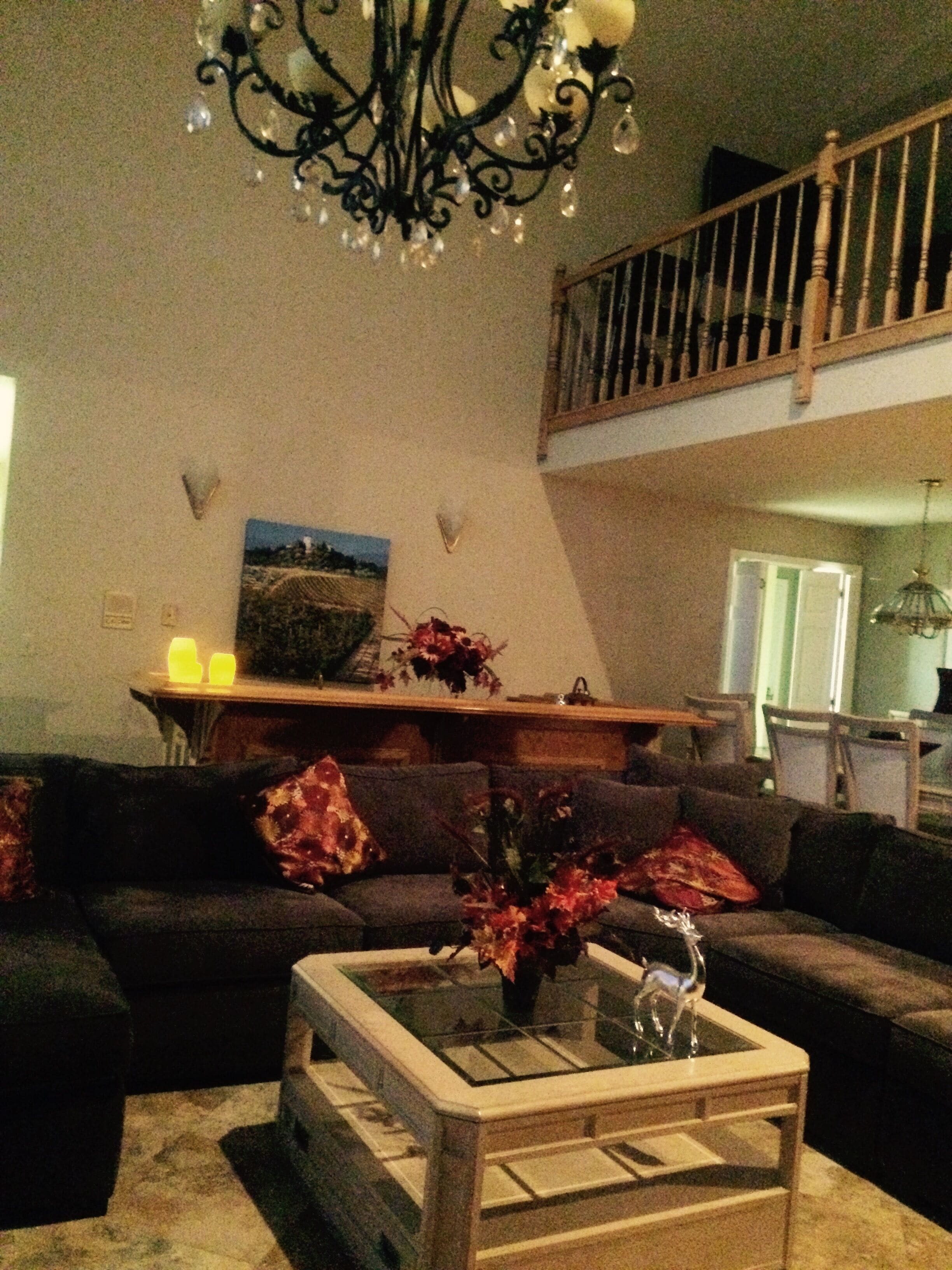 A living room with a dark-colored sofa, a glass-top coffee table, and a chandelier.