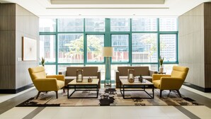 A modern lobby with large windows, a central coffee table, and yellow armchairs. - One Uptown Residence BGC (Taguig)