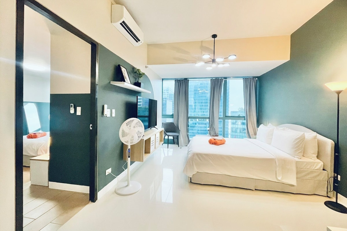 A modern hotel room with a large bed, a desk with a chair, a TV, and a view of the city.