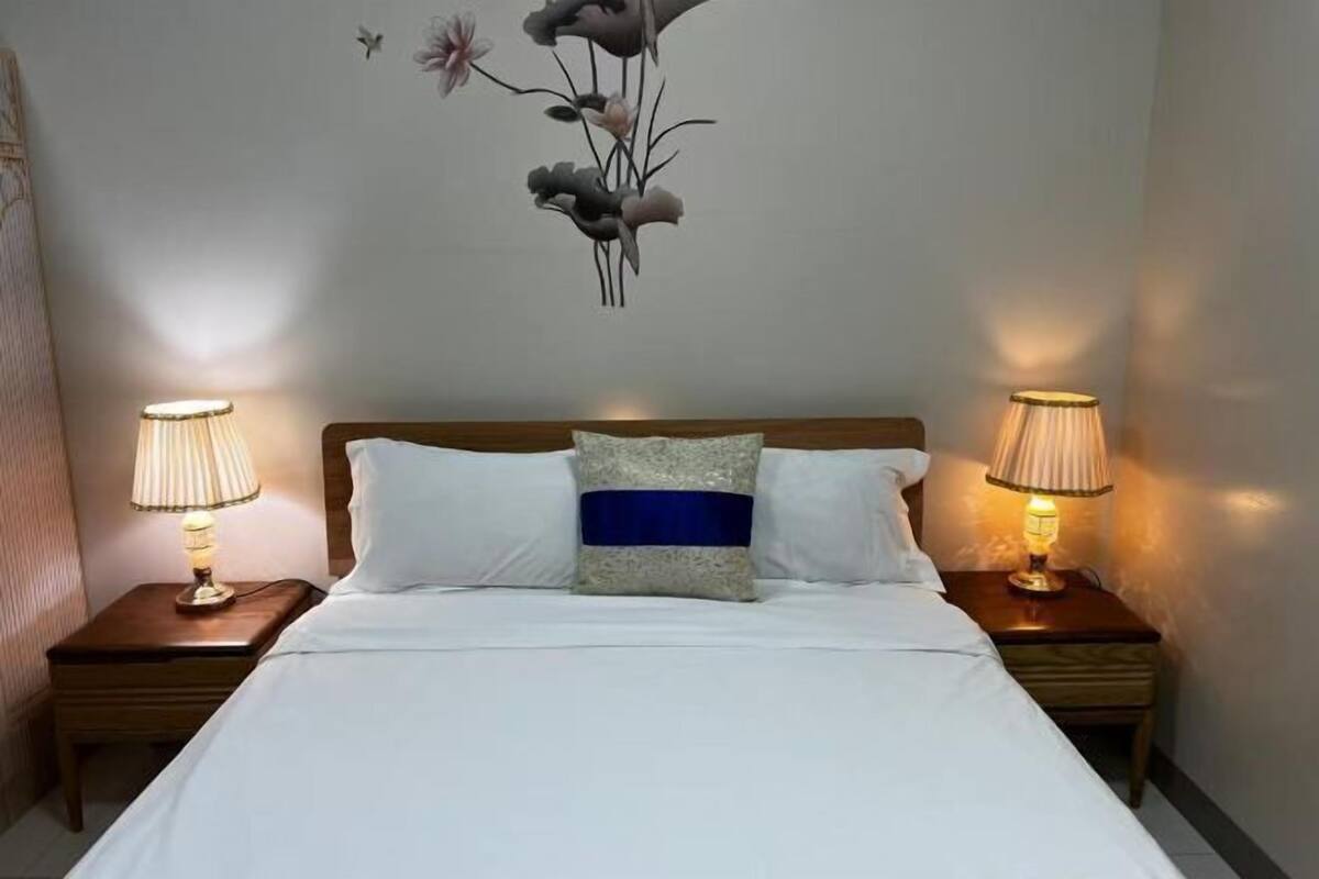 A neatly made bed with white linens, a central pillow with a blue stripe, and two bedside lamps on wooden nightstands.