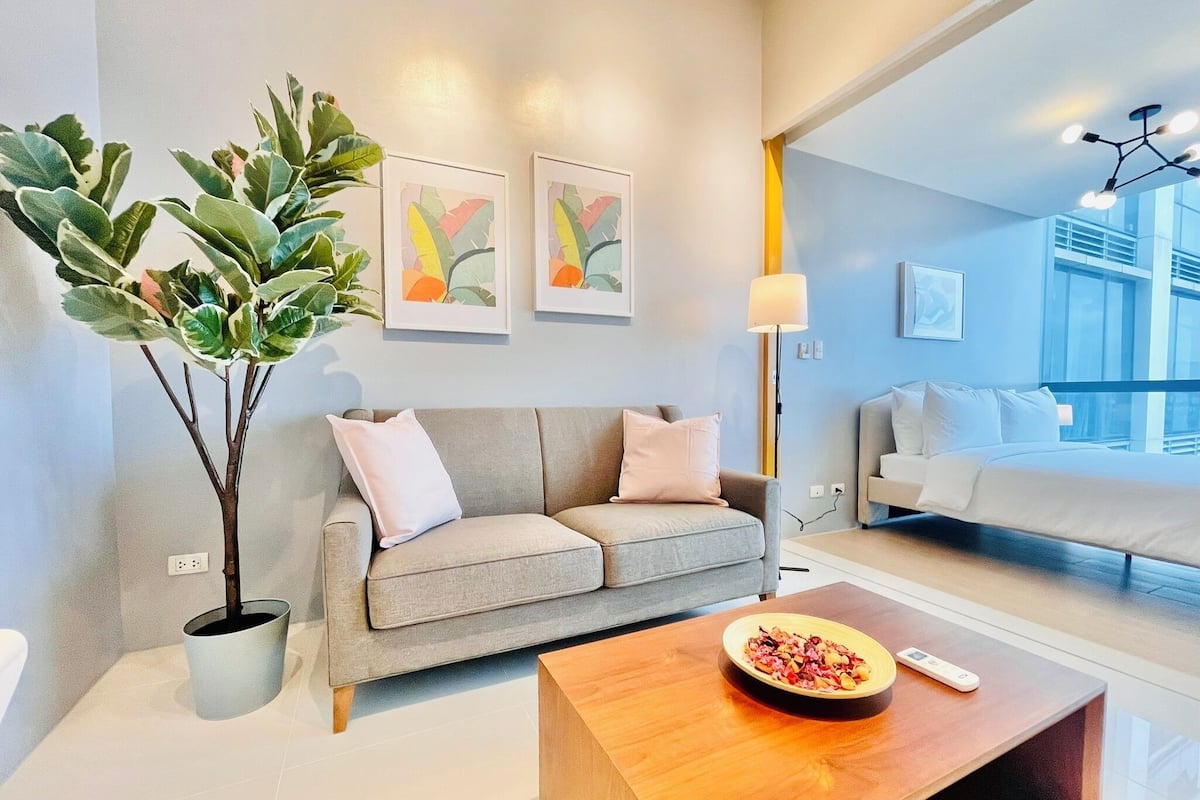 A modern living room with a grey sofa, a coffee table with a bowl of fruit, a potted plant, and artwork on the wall.