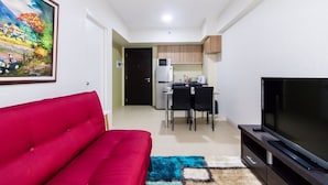 A compact living space with a red sofa, a flat-screen TV, a dining area with a microwave, and a kitchen.