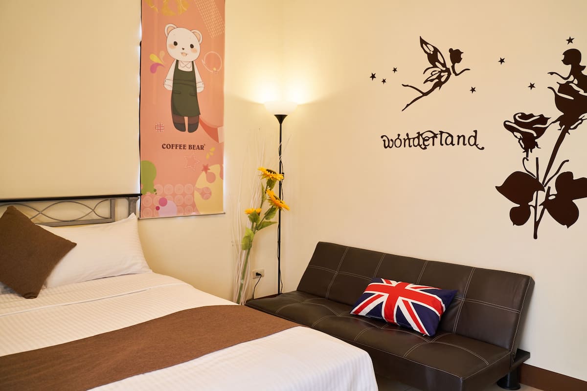 A hotel room with a bed, a sofa, a wall decoration with a bear and the word "wonderland," and a lamp.
