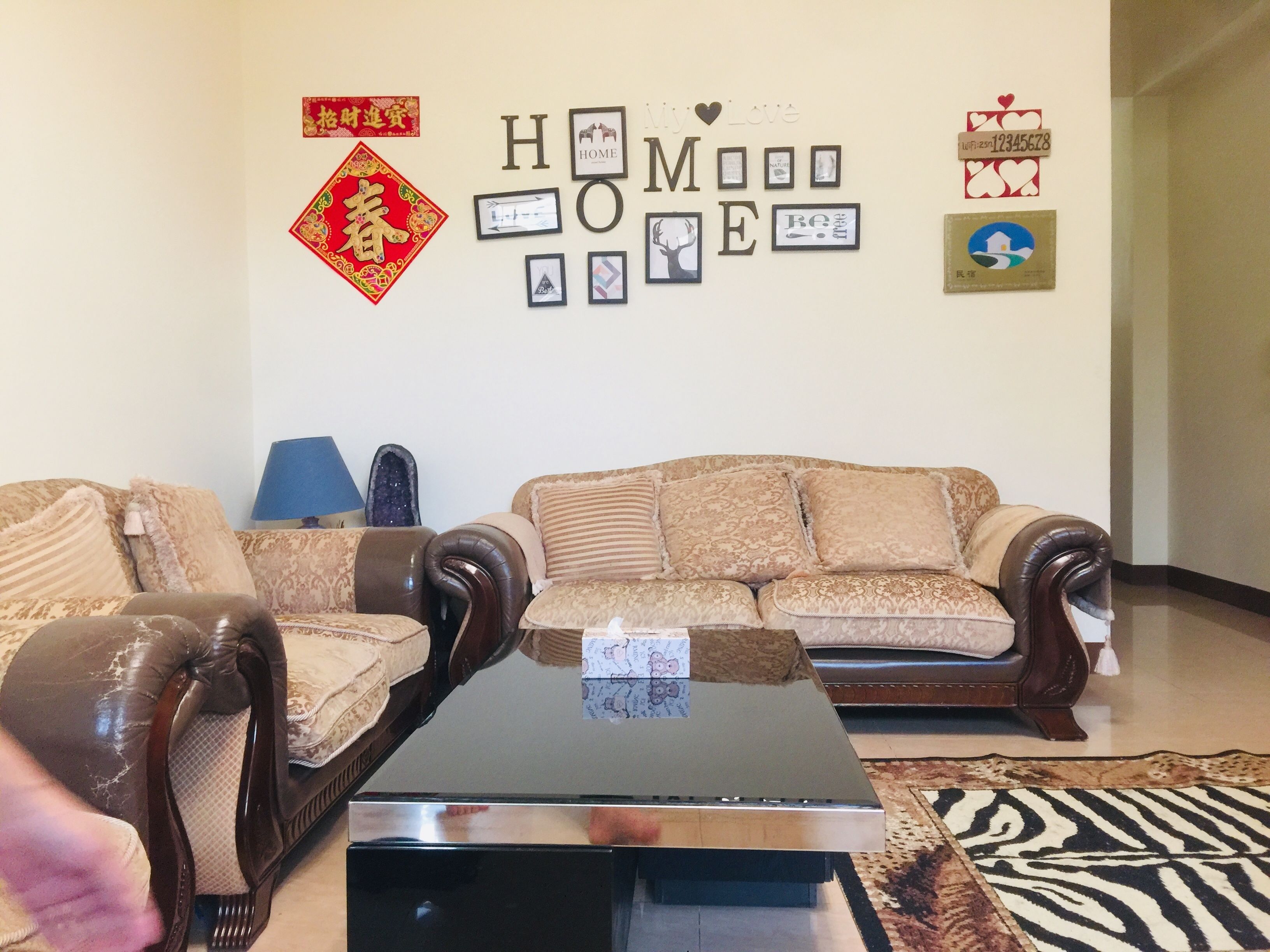 A living room with two sofas, a coffee table, and a wall decorated with framed pictures and a 'HOME' sign.